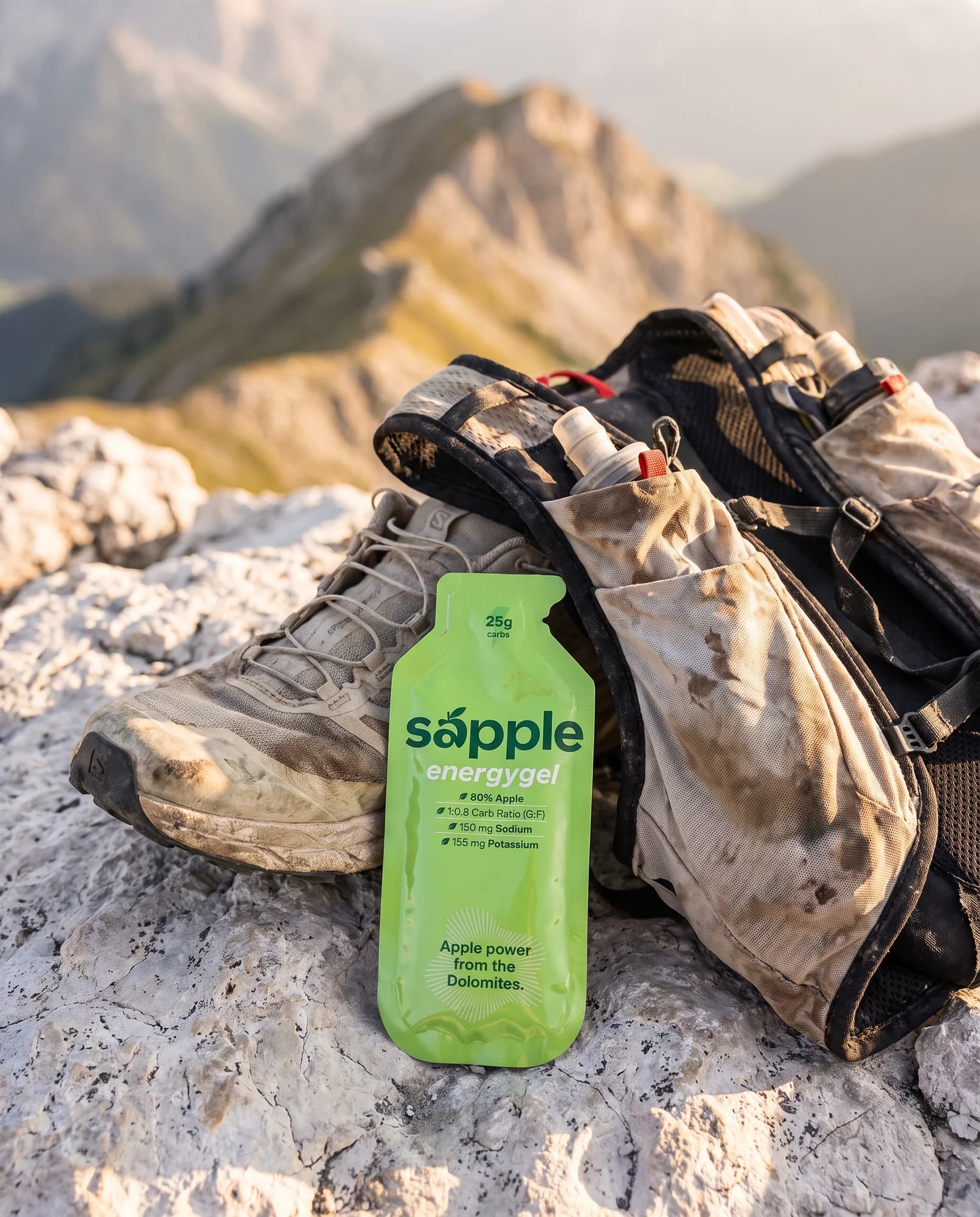 sapple energygel in der neuen Verpackung auf einem Felsen in den Dolomiten, daneben Trailschuhe und Laufrucksack